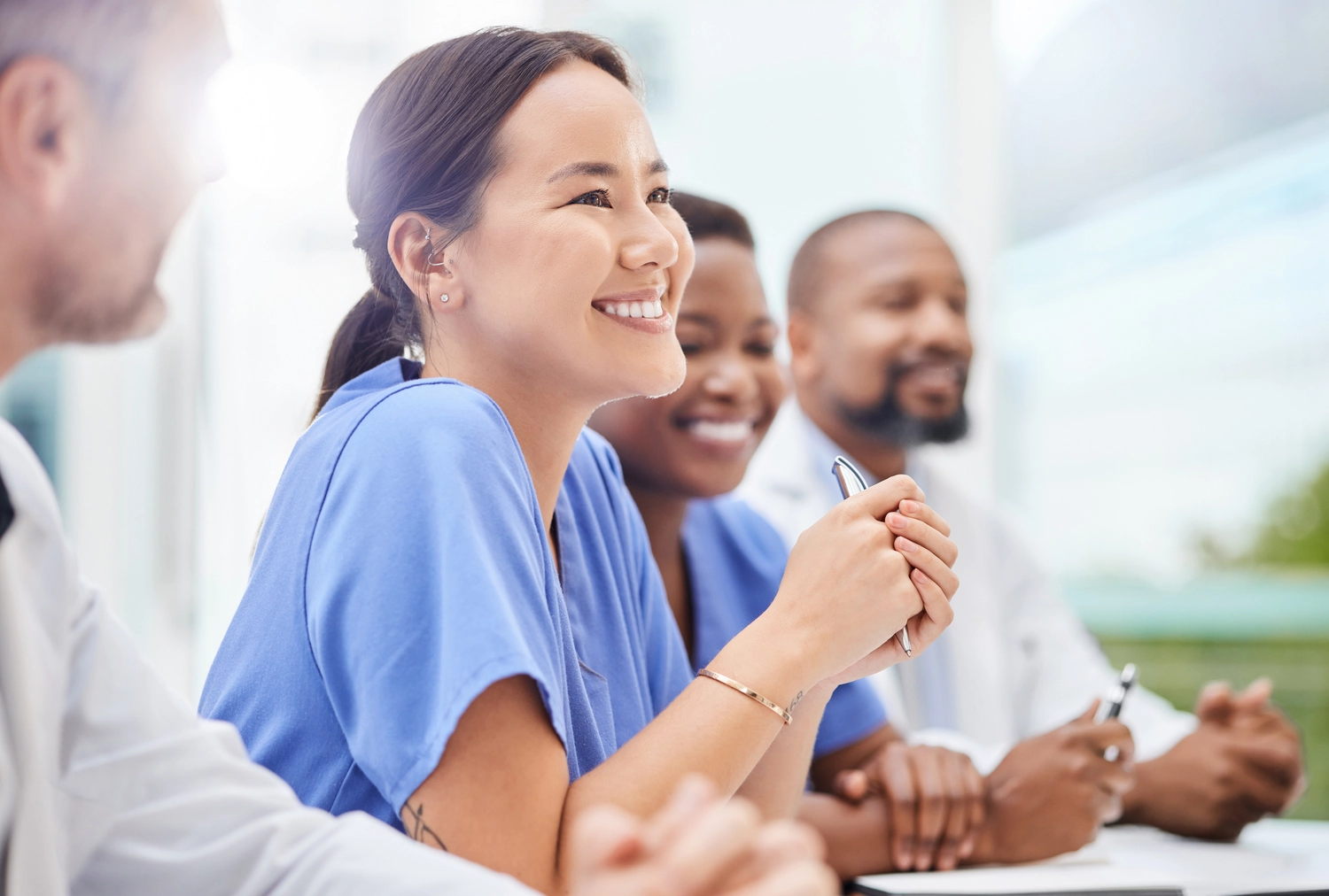 BD Medical Writing & Consulting - Eine Gruppe von medizinischem Fachpersonal unterschiedlicher Fachrichtungen lächelt und hört während einer Besprechung oder Präsentation aufmerksam zu.
